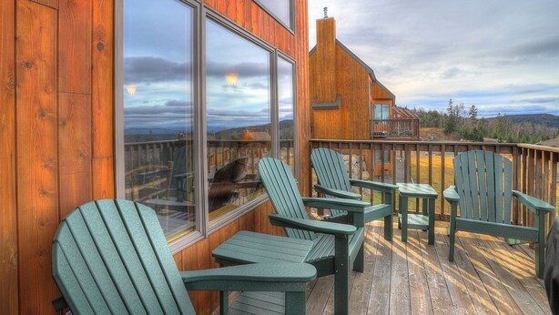 Een houten terras met Adirondack-stoelen en uitzicht op een bergketen.