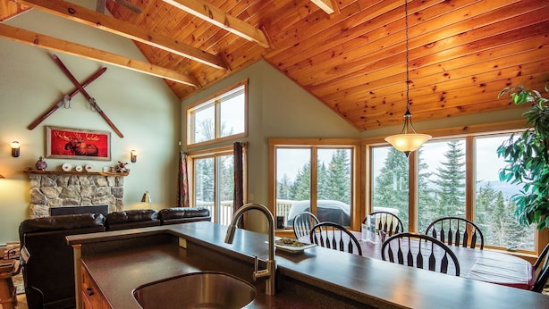 A kitchen with a stone fireplace, wooden ceiling, and large windows overlooking a forest. - Rock Pond Condo 79 | Saddleback, Ski-in/out (Sandy River Plantation)