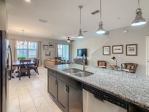 A modern kitchen with granite countertops, a dishwasher, and a dining area with a table and chairs.
