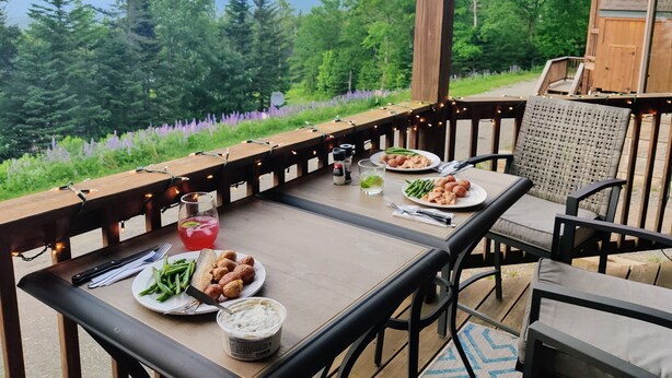Un espace de restauration en plein air avec une table dressée pour deux personnes, entouré de rampes en bois et illuminé de guirlandes lumineuses.