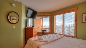 Une chambre à coucher comprenant un lit, une commode, un téléviseur et une fenêtre avec des stores.