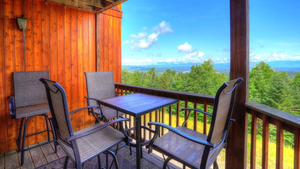 A wooden deck with a table and chairs, overlooking a forested landscape. - South Branch Condo 15-2 - Saddleback Mountain Ski in Ski out condo (Sandy River Plantation)