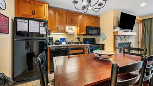 A modern kitchen with wooden cabinets, a stainless steel refrigerator, a microwave, and a dining table with chairs. - South Branch Condo 15-2 - Saddleback Mountain Ski in Ski out condo (Sandy River Plantation)