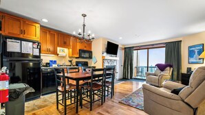 A modern kitchen with wooden cabinets, a black refrigerator, and a dining area with a wooden table and chairs. - South Branch Condo 15-2 - Saddleback Mountain Ski in Ski out condo (Sandy River Plantation)