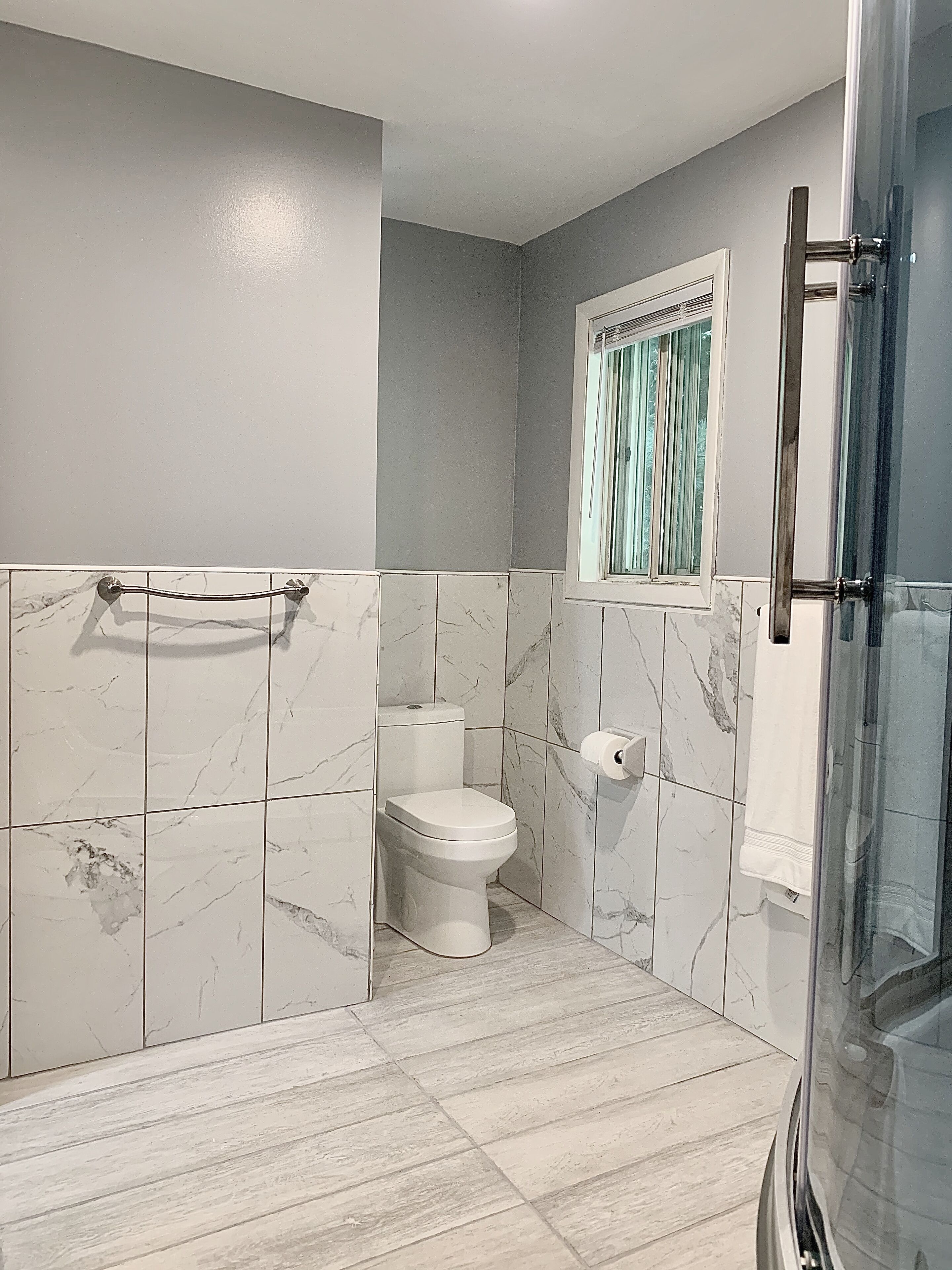 Un baño con inodoro, cabina de ducha de vidrio y pared con azulejos de mármol.