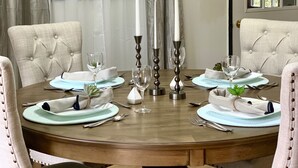 A dining table set for six with a wooden finish, surrounded by upholstered chairs with button detailing.