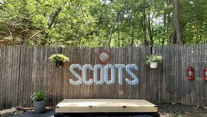 A wooden fence with the word "SCOOTS" painted on it, a small platform, and hanging planters.