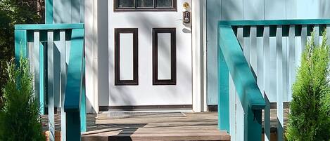 A wooden front door with a small window above it, a mailbox, and a porch with wooden steps and teal railings.