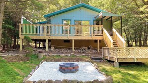 A two-story wooden cabin with a deck and a fire pit in the yard.