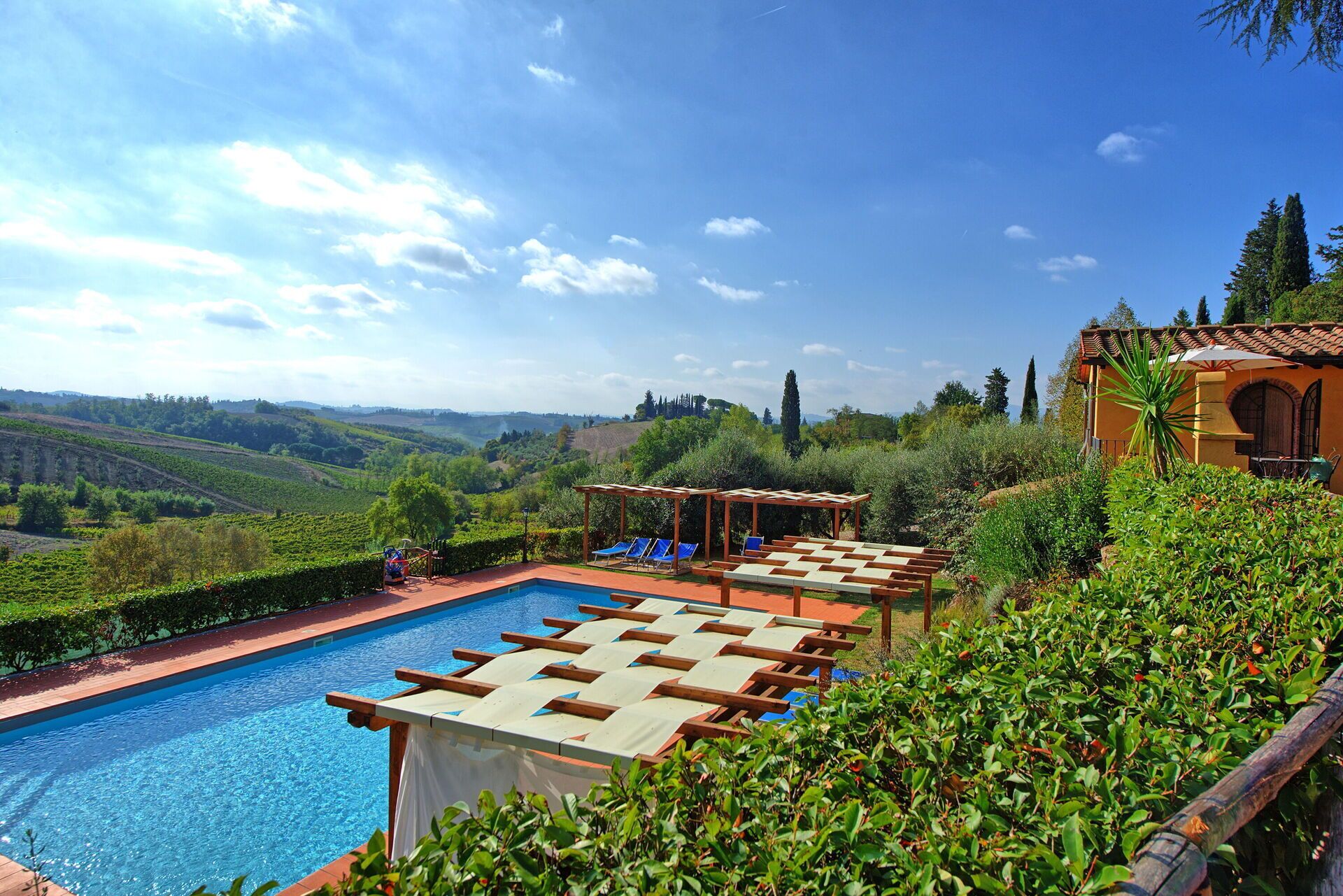 A pool area with lounge chairs, a pergola, and a view of the countryside.
