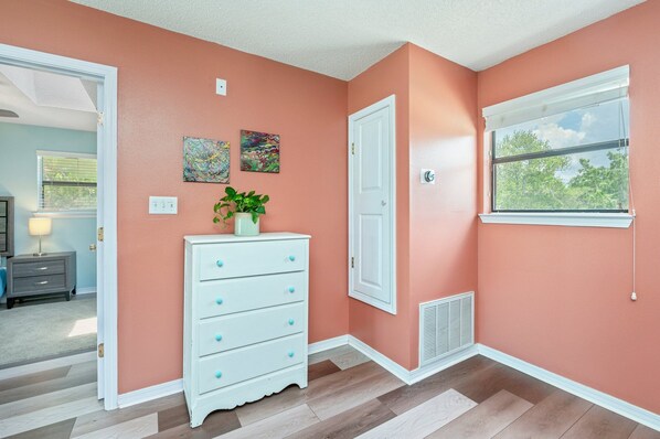 A room with peach walls, a white dresser with drawers, a door, a window with blinds, and two abstract paintings on the wall.