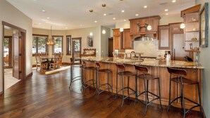 A spacious kitchen with a large island, wooden bar stools, and pendant lighting. - 555 Independence Road by Summit County Mountain Retreats (Keystone)