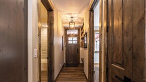 A wooden hallway with a central door, flanked by wooden doors on either side, leading to a room with a window and a chandelier. - The Seasons at Keystone #1819 by Summit County Mountain Retreats (Keystone)
