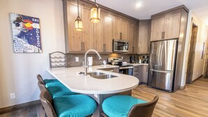 A modern kitchen with wooden cabinets, a stainless steel refrigerator, a built-in oven, and a central island with bar stools. - The Seasons at Keystone #1819 by Summit County Mountain Retreats (Keystone)