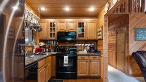 Une cuisine rustique, située dans une cabane en bois, équipée d’une cuisinière, d’un four à micro-ondes et de meubles de rangement en bois.