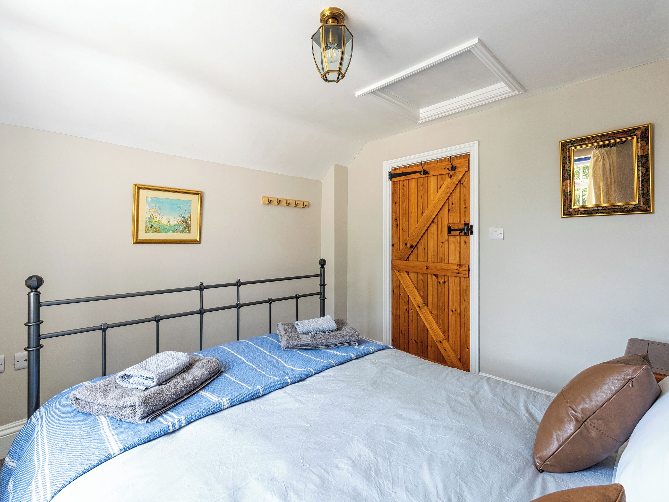 Un dormitorio con una cama, una puerta de madera, un cuadro enmarcado y una lámpara.
