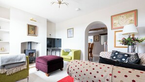 Een woonkamer met een open haard, een bank, een groene fauteuil en een rood vloerkleed.