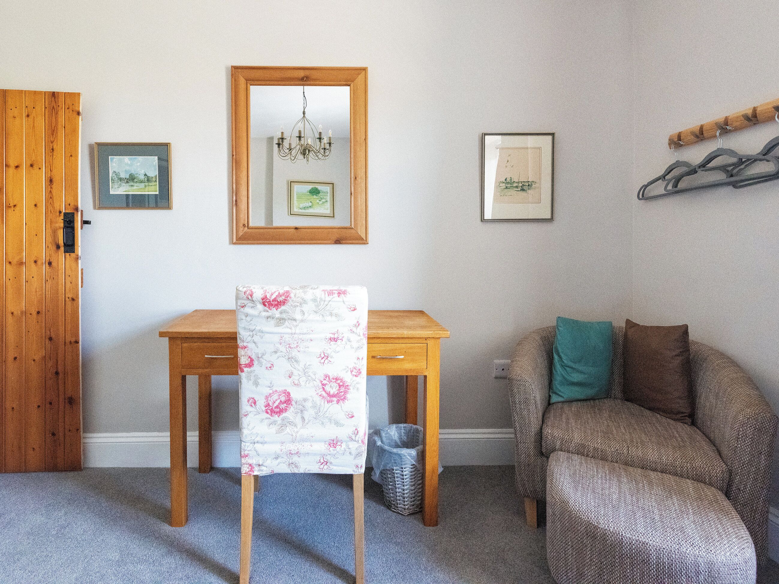 A room with a wooden desk, a chair, a sofa, a mirror, and two framed pictures on the wall.