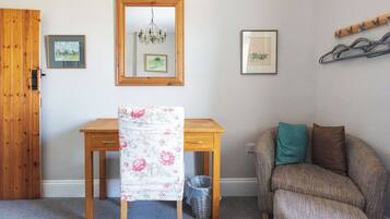 A room with a wooden desk, a chair, a sofa, a mirror, and two framed pictures on the wall.