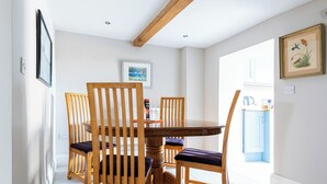 Een eetgedeelte met een ronde houten tafel en vier houten stoelen met kussens.
