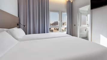 Una habitación de hotel moderna con una cama grande, un televisor de pantalla plana y vistas a la ciudad a través de amplios ventanales.