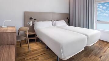 A hotel room with two beds, a desk, a chair, a lamp, and a window with curtains.