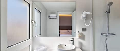 A modern bathroom with a large mirror, a white sink, a handheld showerhead, and a towel on the counter.