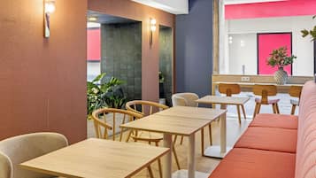 Un interior moderno con mesas y sillas de madera, un sofá rojo y una planta en el alféizar de una ventana.