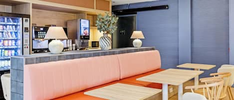 A modern restaurant with a seating area featuring a long bench and tables, a counter with a beverage machine, and a decorative plant.
