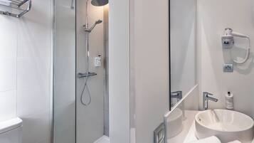 Un baño moderno con ducha envuelta en vidrio, un lavamanos blanco y un cabezal de ducha de mano.