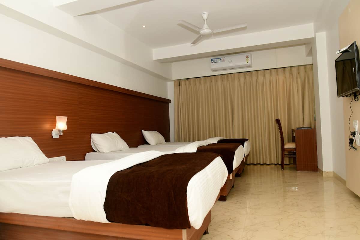 A hotel room with three beds, a ceiling fan, an air conditioning unit, a television, and a desk with a chair.