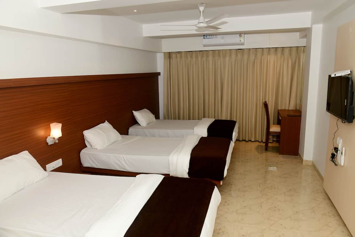 A hotel room with three beds, a ceiling fan, an air conditioning unit, a television, and a desk with a chair.