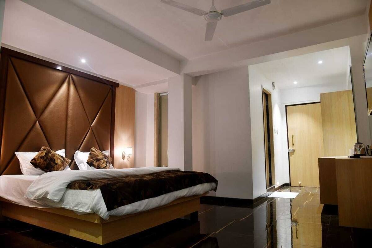 A modern hotel room with a large bed, a wooden headboard, a bedside table, and a mirror.