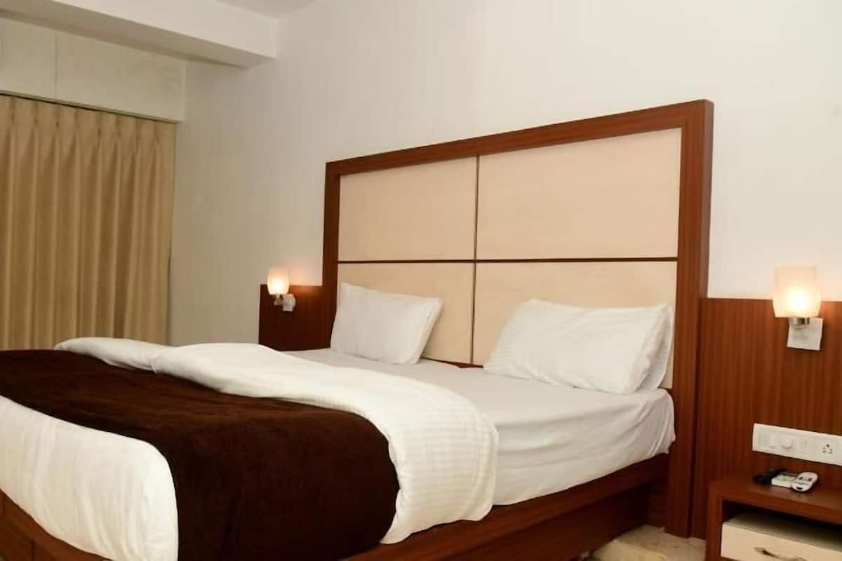 A hotel room with a bed, two bedside tables, a wall-mounted air conditioner, and a curtain.