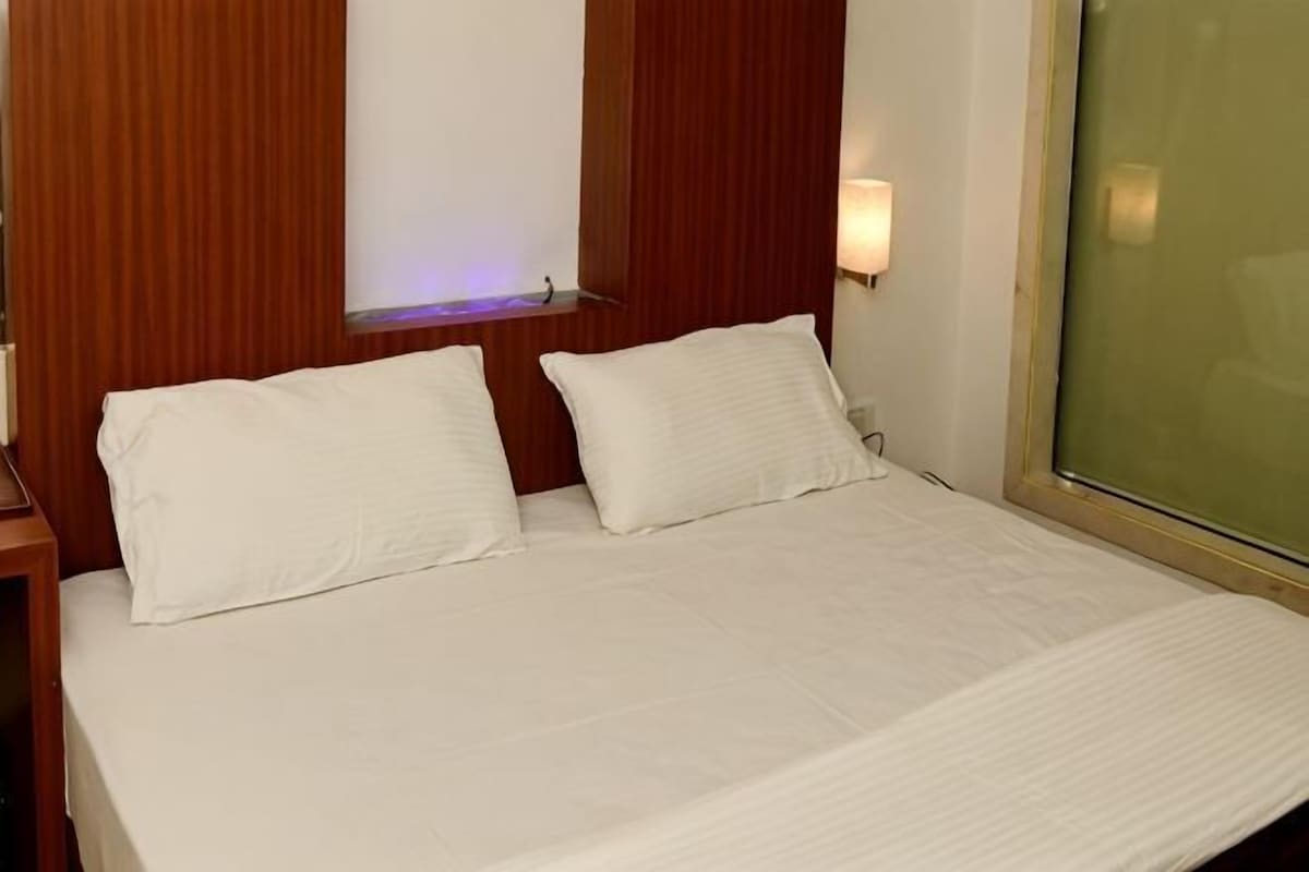 A bed with white linens, a wooden headboard, a bedside table, and a wall-mounted light.
