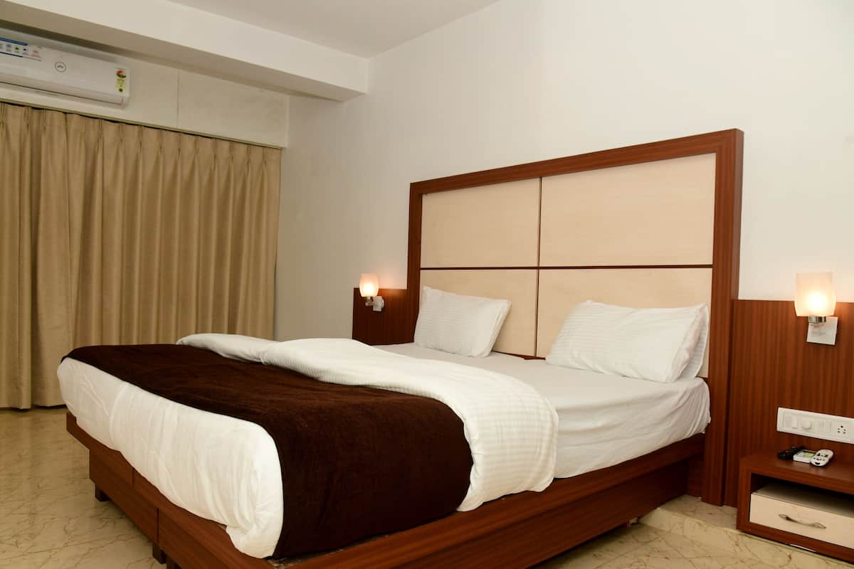 A hotel room with a large bed, wooden headboard, bedside tables with lamps, and an air conditioning unit on the wall.