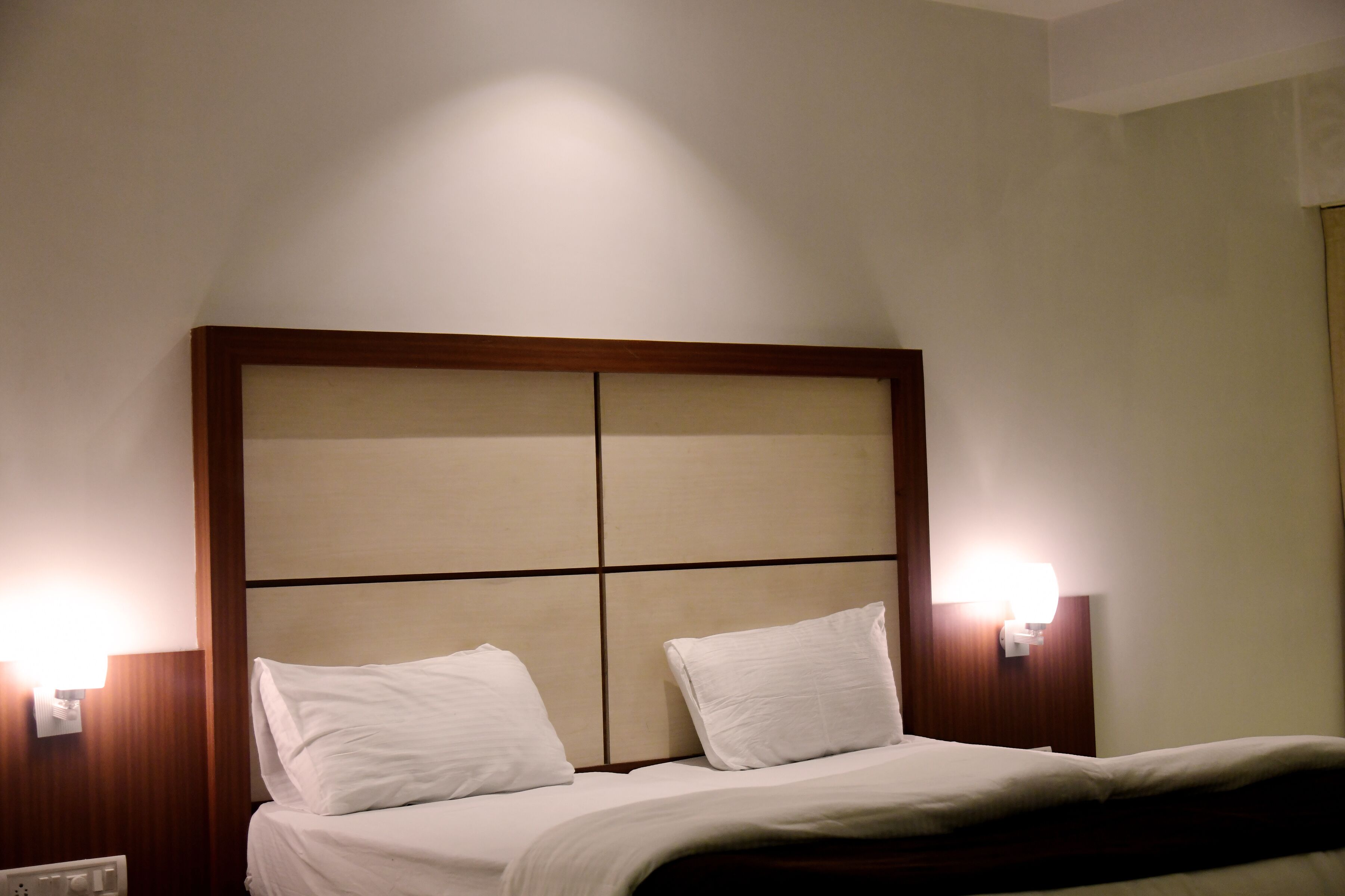 A hotel room with a bed, two bedside lamps, and a wooden headboard.