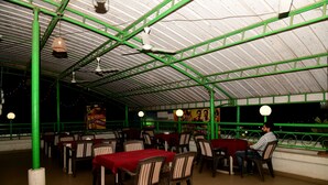 Un restaurant interior amb taules i caires, un sostre metàl·lic verd i llums penjants.