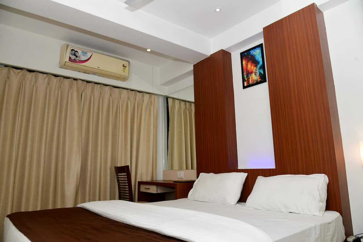 A hotel room with a bed, a desk, a chair, an air conditioning unit, and a painting on the wall.