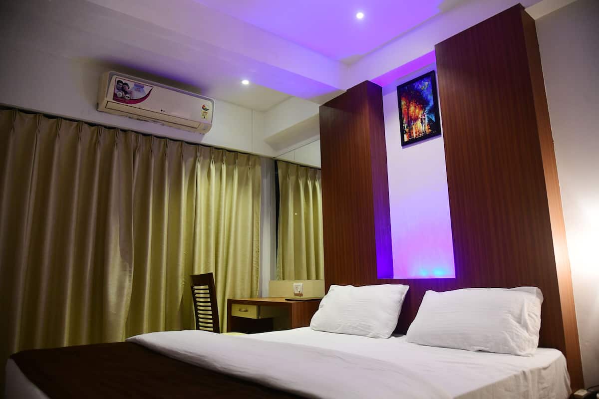 A hotel room with a bed, a desk, a chair, an air conditioning unit, and a wall-mounted artwork.