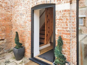 Un bâtiment en briques avec un escalier en bois menant à l’étage supérieur. On peut voir deux plantes en pot au rez-de-chaussée.
