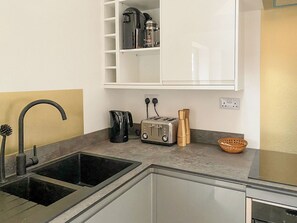 A modern kitchen with a sink, a toaster, a kettle, and a spice rack.