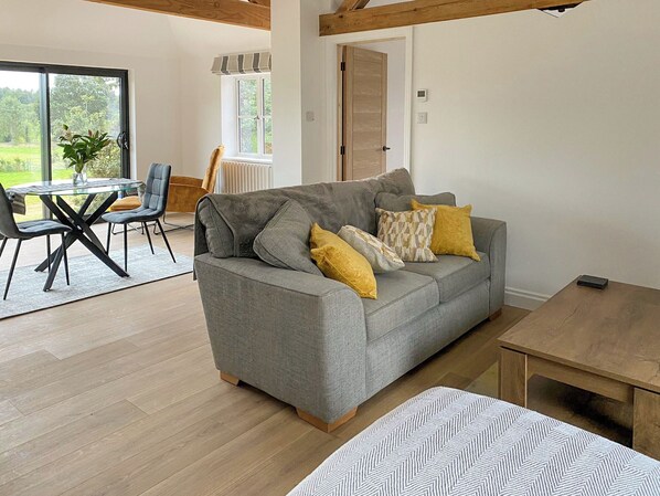 A modern living room with a grey sofa, yellow cushions, a glass coffee table, and a wooden dining table.