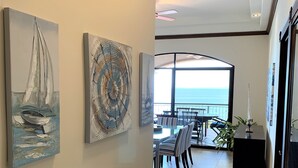 A hallway with artwork on the walls, a dining area with chairs and a table, and a view of the ocean through a large window. - New listing! Stunning views. Fifth floor apartment (Punta Leona)
