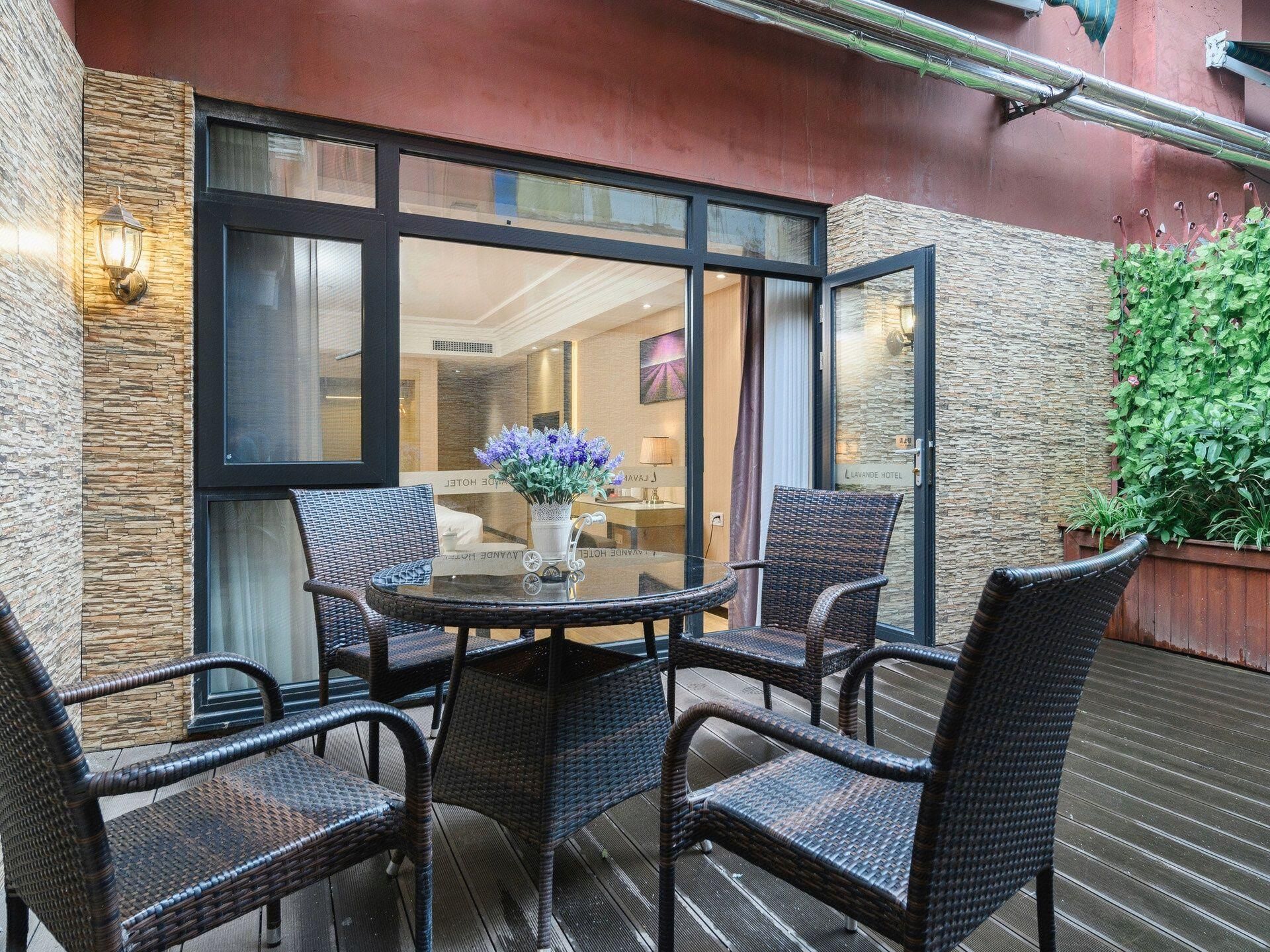 A glass-enclosed outdoor seating area with wicker chairs and a table, a stone wall, and a potted plant.