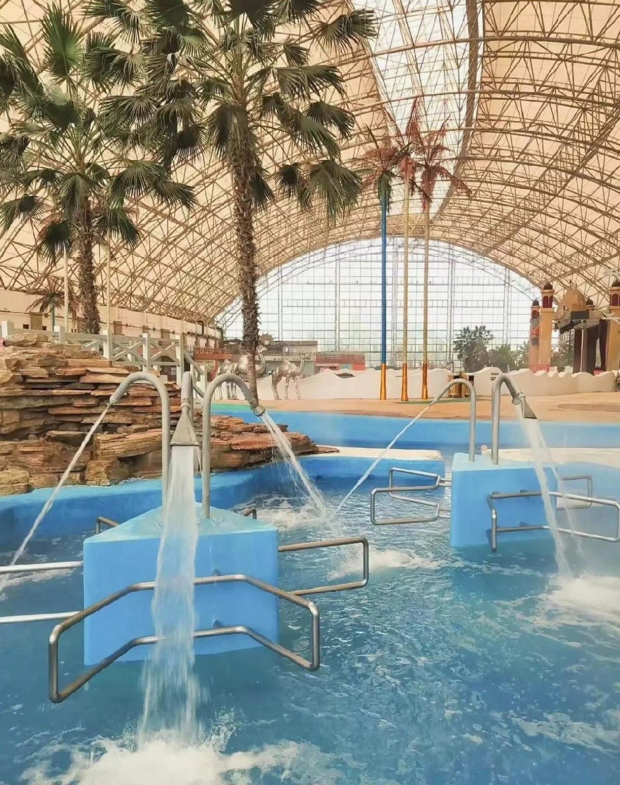 An indoor water park with multiple water slides and a large, arched glass ceiling.