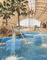 An indoor water park with multiple water slides and a large, arched glass ceiling.