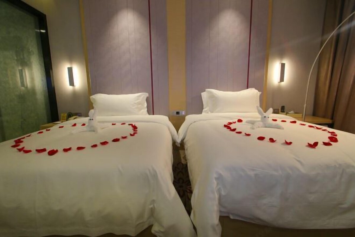 Two adjacent beds with white linens and rose petals arranged in a heart shape on the bed.