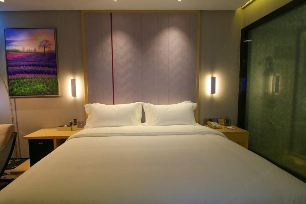 A hotel room with a large bed, bedside tables, a nightstand, a lamp, and a painting on the wall.