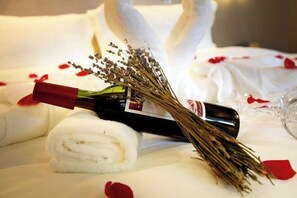 A bottle of wine, a bouquet of dried flowers, and a rolled towel on a bed with rose petals. - Lavande Hotel (Guangyuan Wanda Plaza Olympic Center) (Guangyuan)
